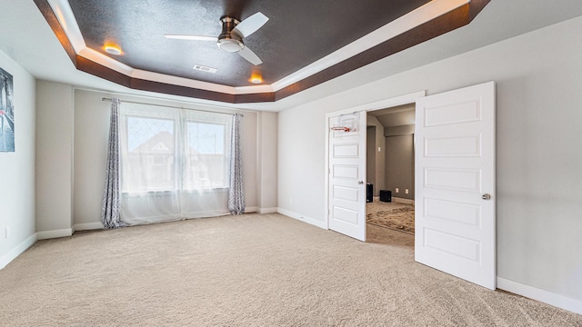 unfurnished bedroom with ceiling fan, a tray ceiling, and carpet flooring