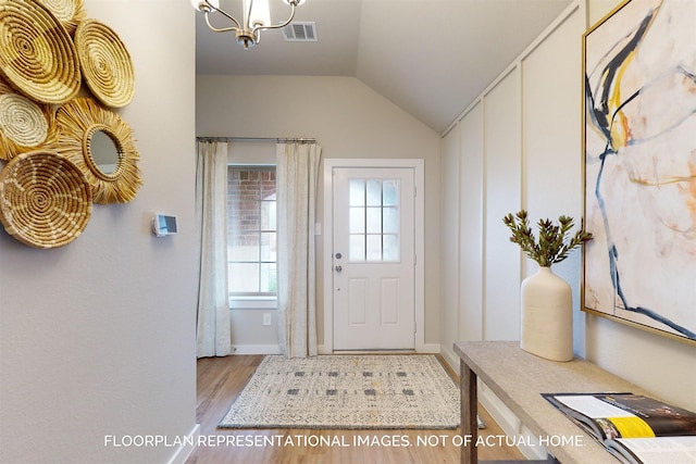 entryway with lofted ceiling, an inviting chandelier, light wood-style flooring, and visible vents