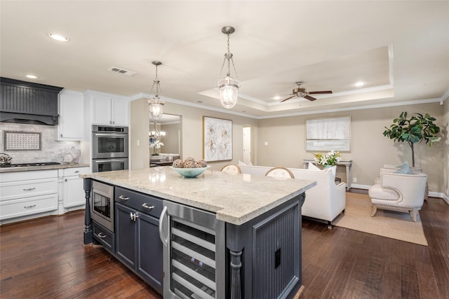 kitchen featuring stainless steel appliances, a center island, a raised ceiling, and wine cooler