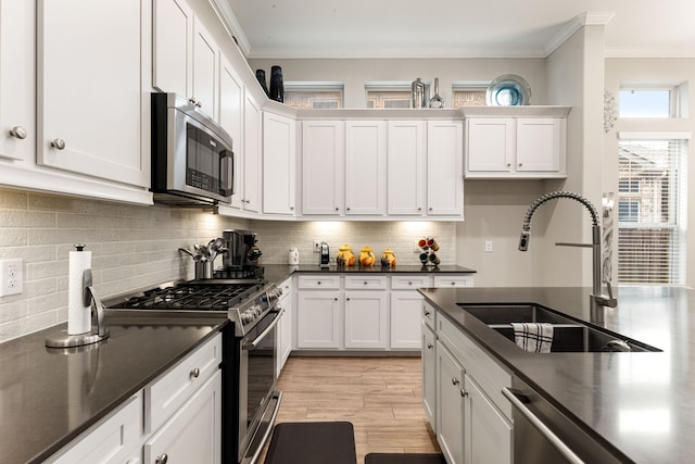 kitchen featuring white cabinetry, stainless steel appliances, decorative backsplash, sink, and ornamental molding