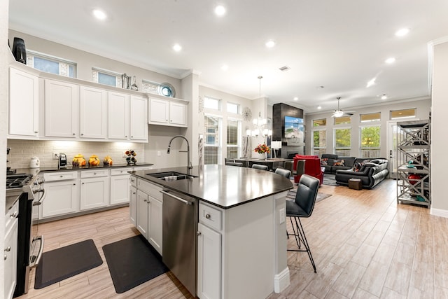 kitchen with sink, crown molding, white cabinetry, a kitchen island with sink, and stainless steel appliances