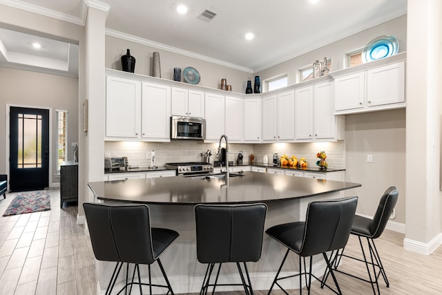 kitchen with a center island with sink, appliances with stainless steel finishes, a healthy amount of sunlight, white cabinets, and sink