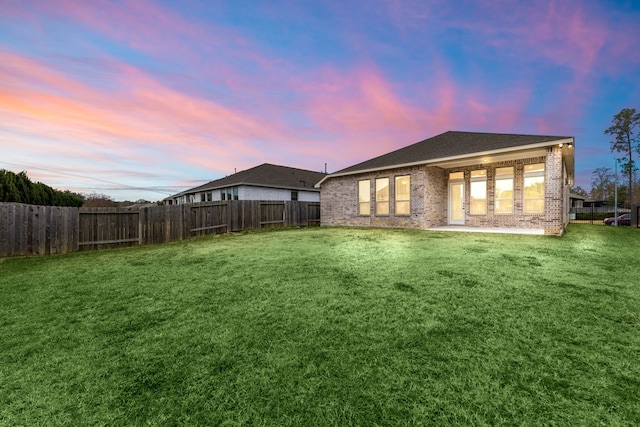 back house at dusk with a patio area and a yard