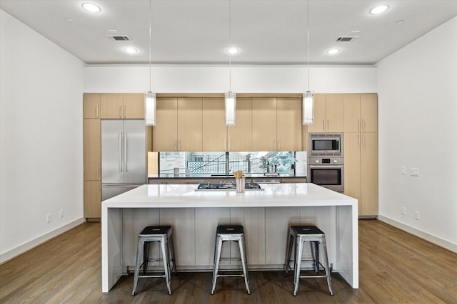 kitchen with a kitchen bar, decorative light fixtures, built in appliances, and an island with sink