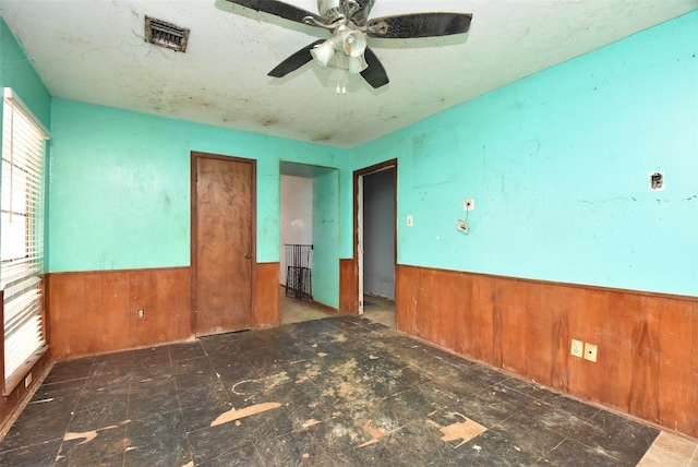 empty room featuring ceiling fan and wooden walls