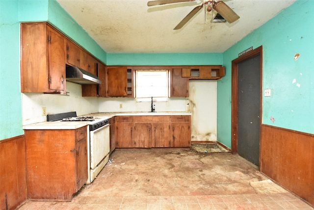 kitchen featuring ceiling fan, sink, wooden walls, and white gas range oven