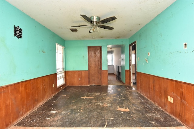 spare room featuring ceiling fan, a healthy amount of sunlight, and wooden walls