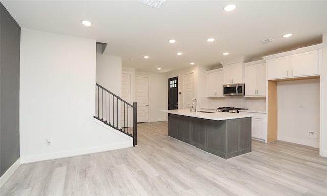 kitchen featuring sink, white cabinetry, light hardwood / wood-style floors, an island with sink, and decorative backsplash