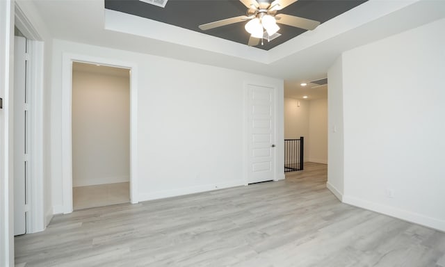 empty room with ceiling fan, light wood-type flooring, and a tray ceiling