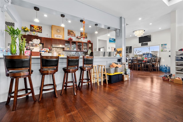 kitchen featuring decorative light fixtures, dark hardwood / wood-style floors, kitchen peninsula, decorative backsplash, and a kitchen bar