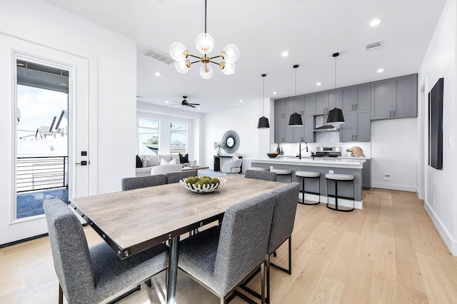 dining room with light wood-type flooring, ceiling fan with notable chandelier, and sink