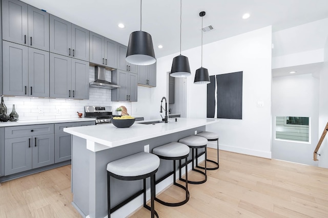 kitchen featuring decorative light fixtures, sink, wall chimney range hood, and an island with sink