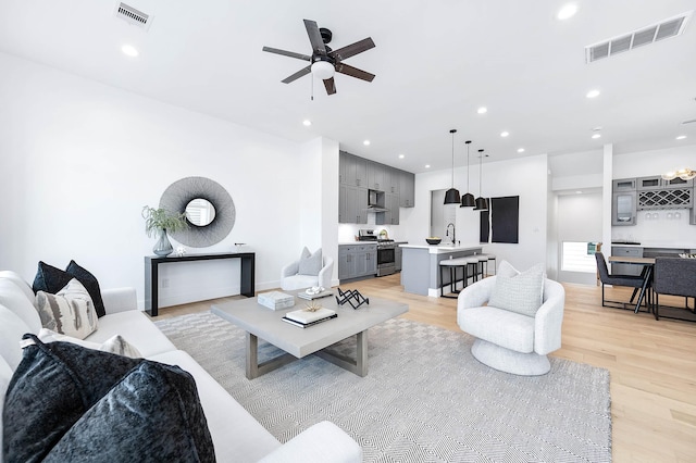 living room featuring ceiling fan, sink, and light hardwood / wood-style flooring