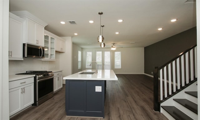 kitchen with a center island with sink, stainless steel appliances, decorative light fixtures, white cabinets, and sink