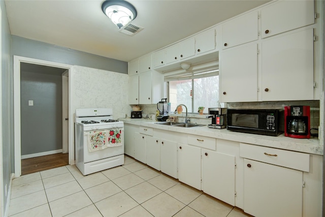 kitchen featuring light tile patterned flooring, white gas range, white cabinets, and sink