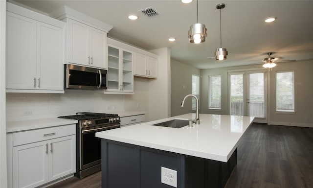 kitchen with an island with sink, appliances with stainless steel finishes, decorative light fixtures, white cabinets, and sink