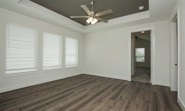 empty room with a raised ceiling, ceiling fan, and dark wood-type flooring