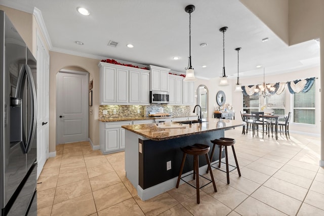 kitchen featuring hanging light fixtures, dark stone countertops, an island with sink, stainless steel appliances, and white cabinets