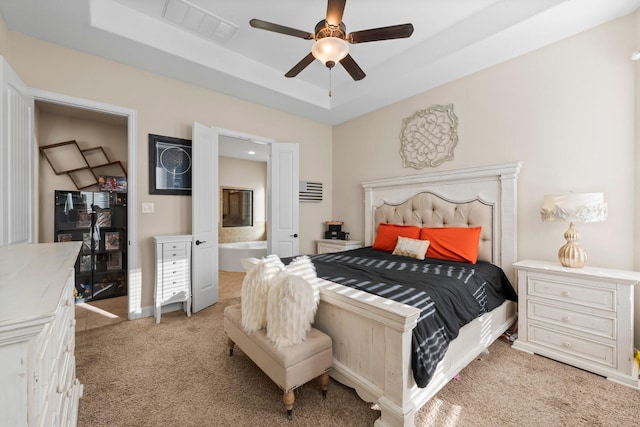 bedroom featuring ceiling fan, ensuite bathroom, a tray ceiling, and light colored carpet