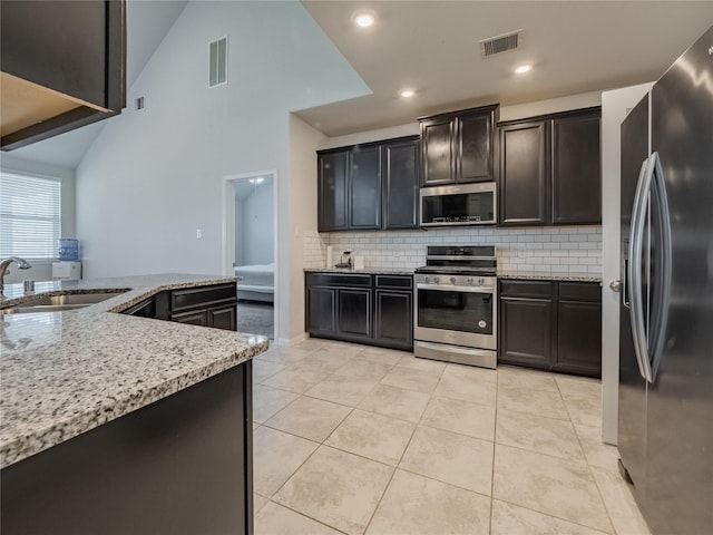 kitchen with sink, tasteful backsplash, light tile patterned floors, appliances with stainless steel finishes, and light stone countertops