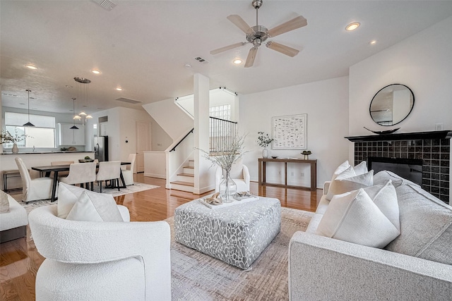 living room with a tile fireplace, ceiling fan, and light hardwood / wood-style floors