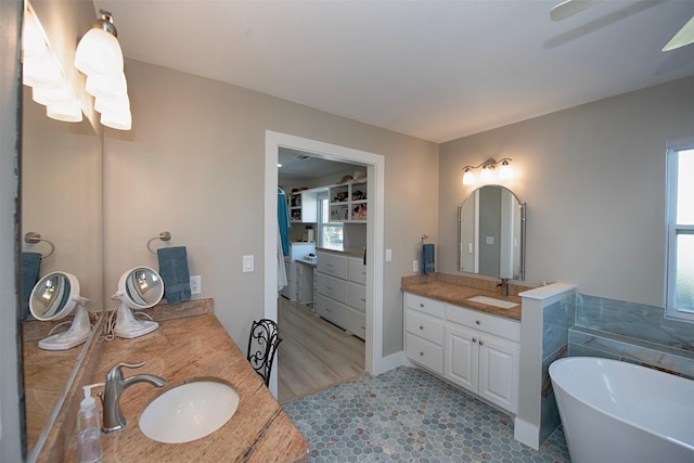 bathroom featuring plenty of natural light, a soaking tub, two vanities, and a sink