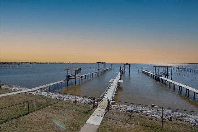 dock area with a water view, boat lift, and fence