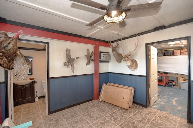 below grade area featuring a textured ceiling, wainscoting, ceiling fan, and a wall mounted air conditioner