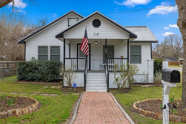 bungalow-style home with covered porch, metal roof, a front lawn, and fence