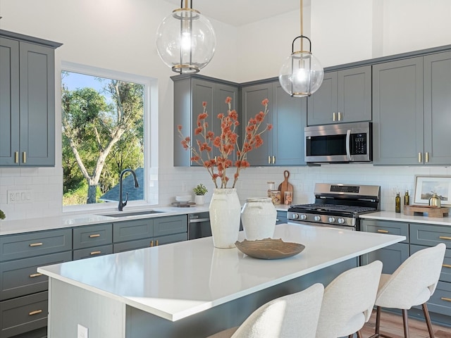 kitchen featuring gray cabinets, stainless steel appliances, hanging light fixtures, and sink