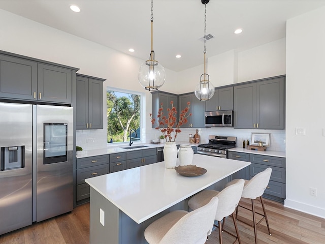 kitchen featuring pendant lighting, appliances with stainless steel finishes, a center island, tasteful backsplash, and sink