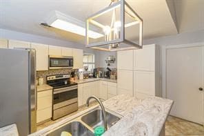 kitchen with appliances with stainless steel finishes, a chandelier, light stone counters, and sink