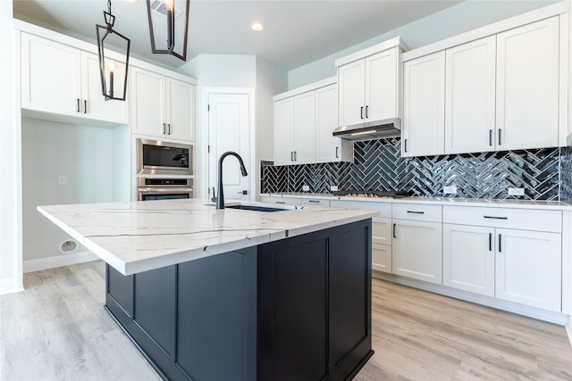 kitchen with white cabinetry, stainless steel appliances, a center island with sink, and sink