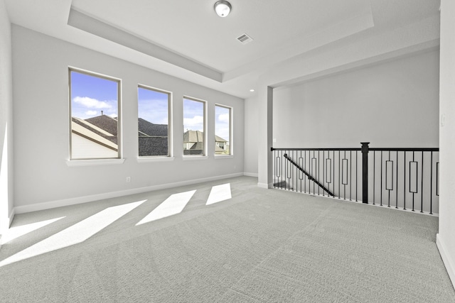 carpeted empty room featuring a tray ceiling, baseboards, and visible vents