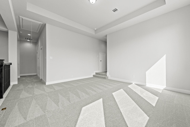 empty room featuring attic access, light colored carpet, visible vents, and a tray ceiling