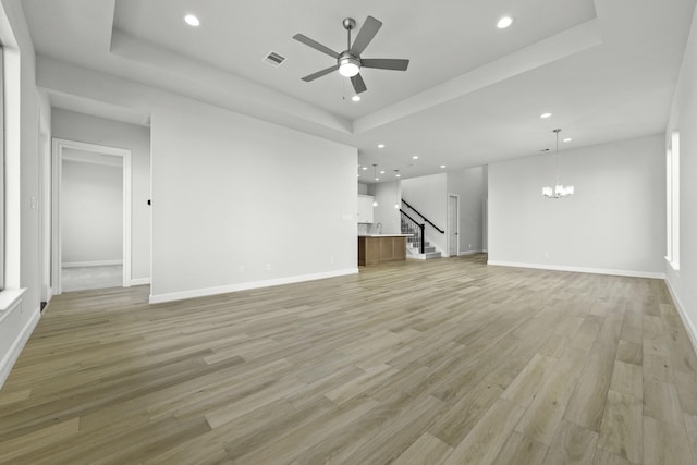 unfurnished living room featuring light wood-type flooring, a tray ceiling, recessed lighting, and ceiling fan with notable chandelier