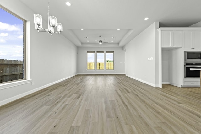 unfurnished living room with recessed lighting, light wood-style flooring, a raised ceiling, and baseboards