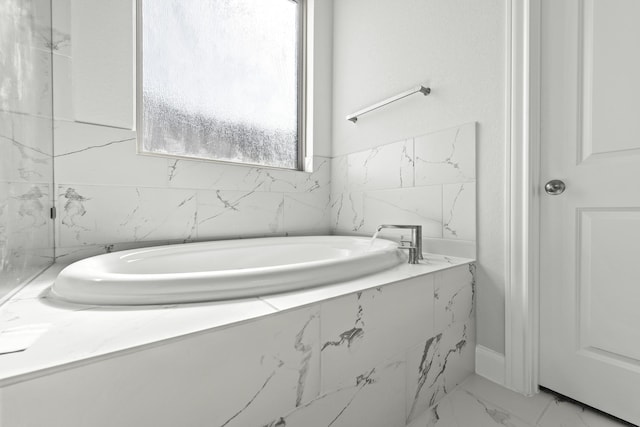 bathroom with a garden tub and marble finish floor