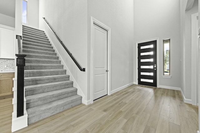 foyer featuring light wood finished floors, stairs, a high ceiling, and baseboards