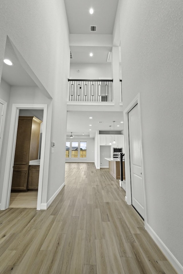 corridor with visible vents, baseboards, recessed lighting, light wood-style floors, and a towering ceiling