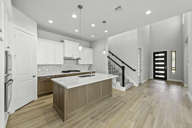 kitchen with visible vents, a sink, decorative backsplash, light wood-style floors, and under cabinet range hood