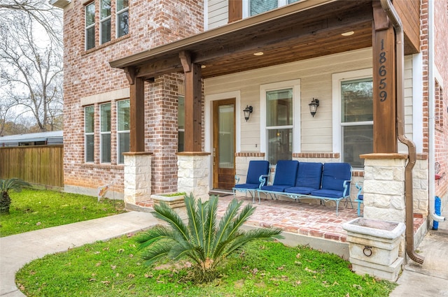 property entrance with covered porch, fence, and brick siding