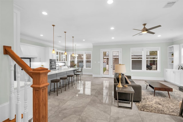 living room with ceiling fan with notable chandelier, built in shelves, ornamental molding, and french doors