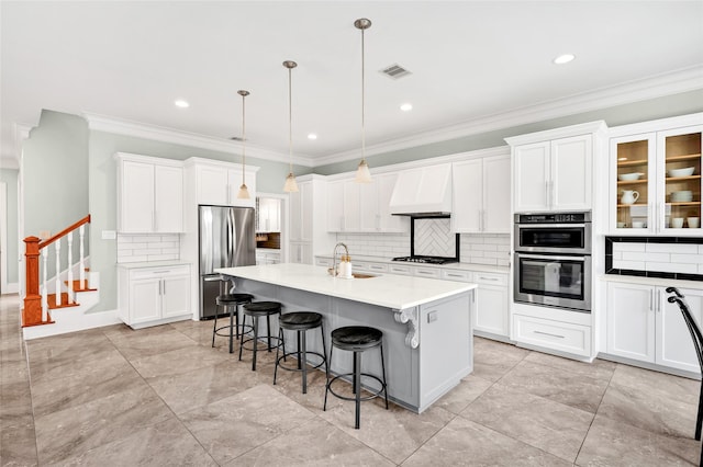 kitchen featuring custom range hood, decorative light fixtures, a kitchen bar, a center island with sink, and stainless steel appliances