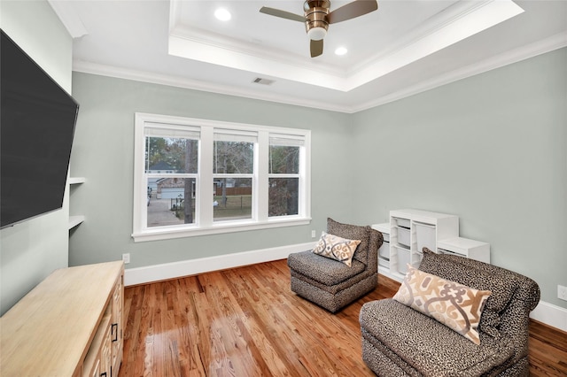 living area with crown molding, light hardwood / wood-style flooring, a tray ceiling, and ceiling fan