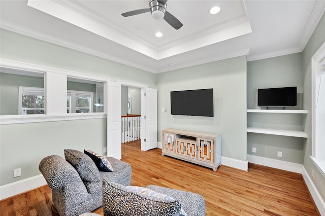 living room featuring hardwood / wood-style flooring, ornamental molding, a raised ceiling, and ceiling fan