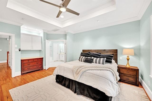 bedroom featuring ensuite bathroom, light hardwood / wood-style floors, ornamental molding, ceiling fan, and a tray ceiling