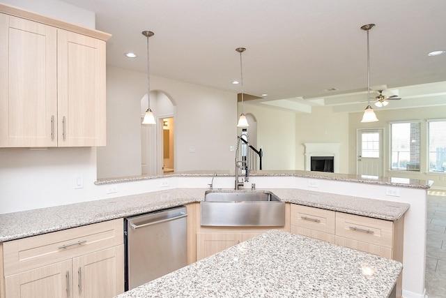 kitchen featuring pendant lighting, light brown cabinetry, sink, stainless steel dishwasher, and light stone counters