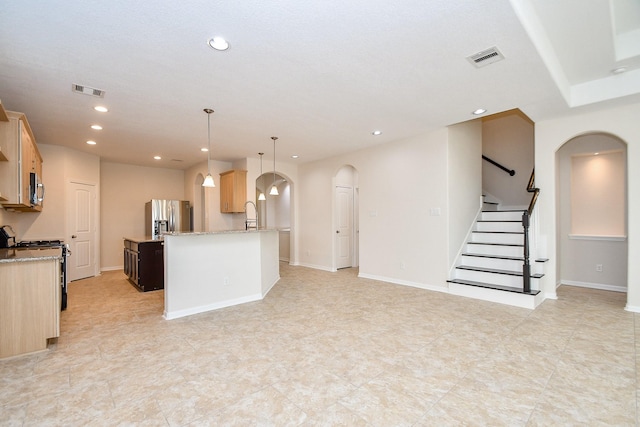 kitchen featuring pendant lighting, appliances with stainless steel finishes, light stone countertops, an island with sink, and light brown cabinets