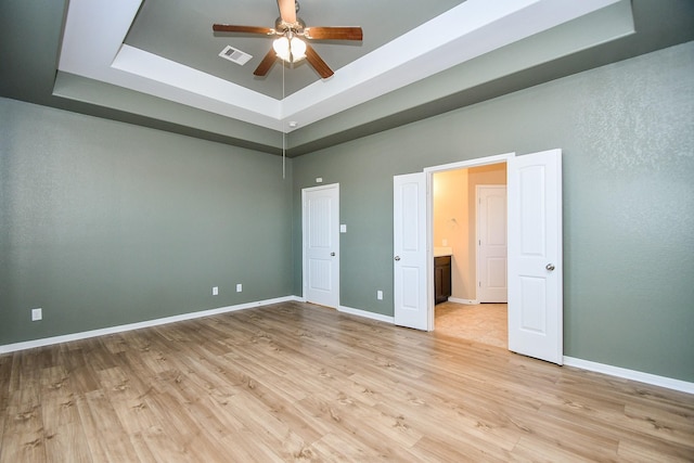 unfurnished bedroom with a tray ceiling, light wood-type flooring, ceiling fan, and a towering ceiling